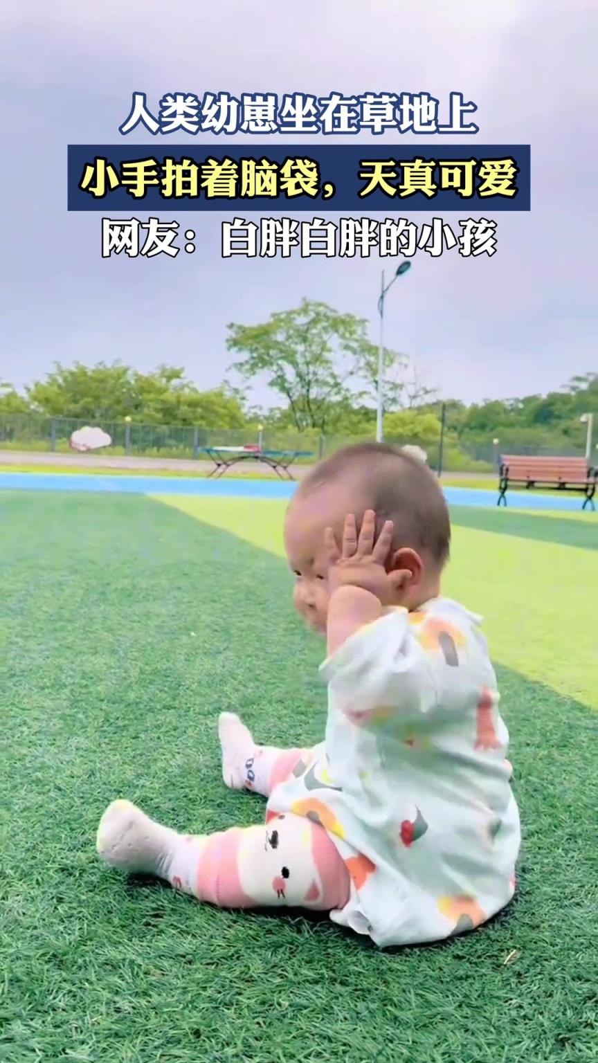 人类幼崽坐在草地上，小手拍着脑袋，天真可爱